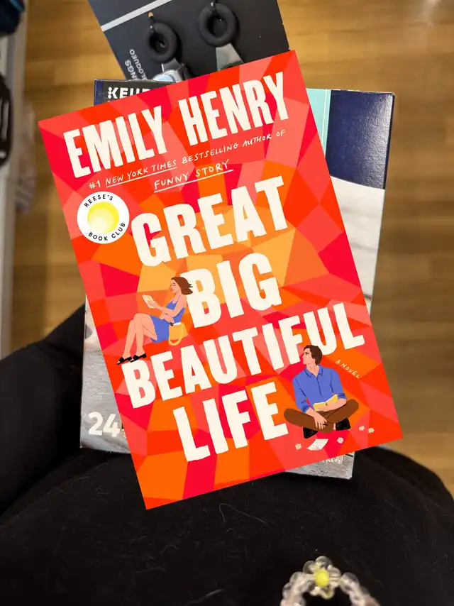 The book cover for "Great Big Beautiful Life" by Emily Henry, featuring a colorful geometric design and a "Reese's Book Club" sticker, placed on a dark surface.